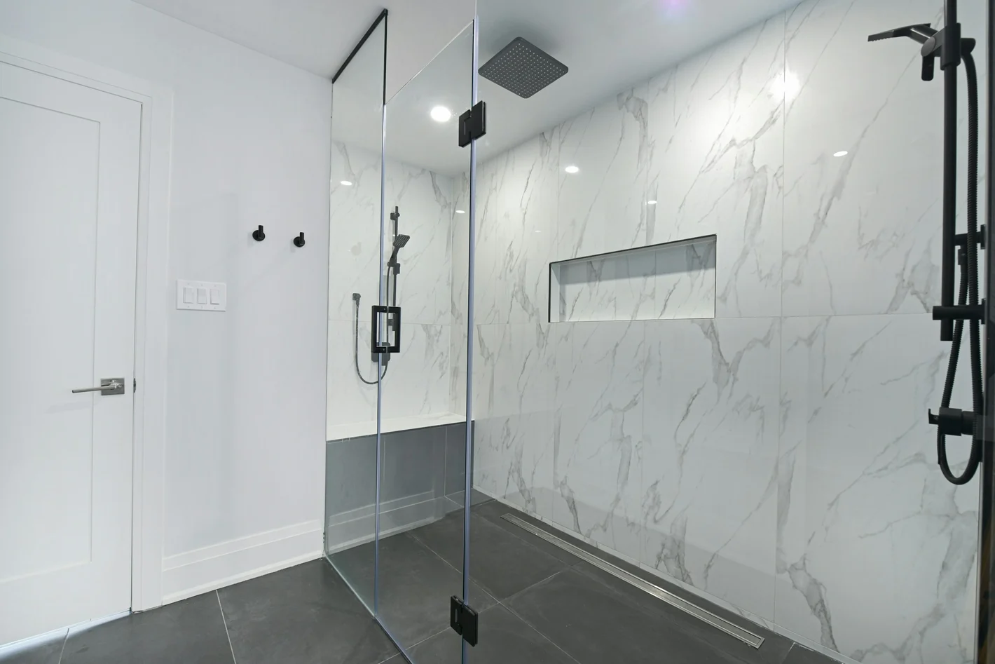 Glass-enclosed shower with marble-look porcelain wall tile, a recessed niche, and a linear drain