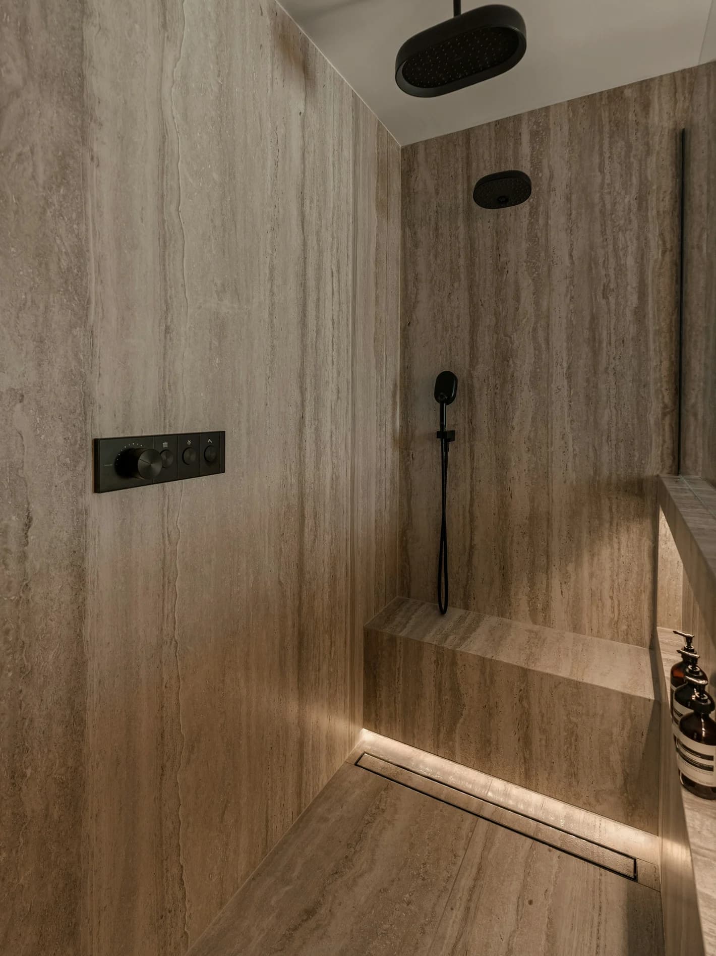 Walk-in shower clad in vein-cut travertine-look tile with a built-in bench and linear drain
